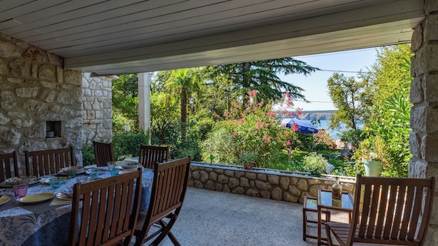 Eine Terrasse im Freien mit Steinmauern, Holzsesseln und einem für das Essen gedeckten Tisch.