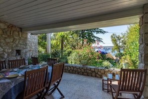Une terrasse extérieure avec des murs en pierre, des chaises en bois et une table dressée pour le repas.