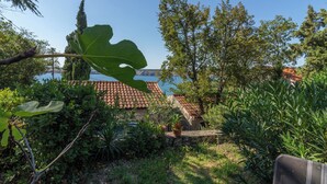 Ein Garten mit Steinmauer, einem großen Blatt und Blick auf ein Gebäude mit Ziegeldach.
