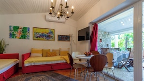 Ein modernes Wohnzimmer mit einem roten Sofa, einem Esstisch mit Stühlen, einer Chandelüster und Kunstwerken an den Wänden.