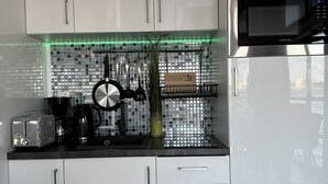 Una cocina moderna con armarios blancos, un microondas de acero inoxidable y un salpicadero con baldosas reflectantes.