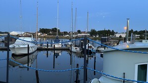 Un puerto deportivo con barcos amarrados, un pequeño edificio con ventanal y un muelle con una persona sentada en una silla.