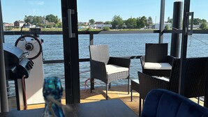 Una terraza con mesa y sillas que da a una masa de agua, un timón y una botella.