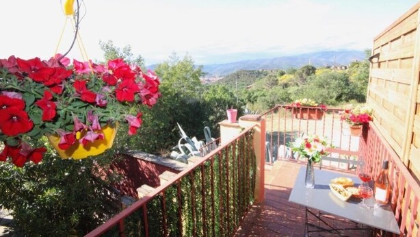 Ein Balkon mit einem hängenden Blumentopf, einem Tisch mit einer Flasche und Gläsern sowie Blick auf die Landschaft.