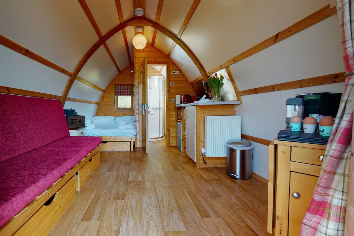 A cozy, compact room with a wooden ceiling, a red sofa, a small kitchenette, and a shower.