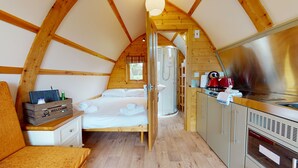 Una habitación acogedora con paneles de madera, una cama, un escritorio pequeño, una kitchenette y un baño con ducha.