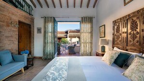 A bedroom with a large bed, a wooden headboard, a blue sofa, and a view of the outside balcony. - La Esperanza Granada (El Valle)