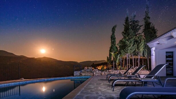 A poolside area with lounge chairs and a stone deck, overlooking a mountainous landscape with a pool reflecting the moonlight. - La Esperanza Granada (El Valle)