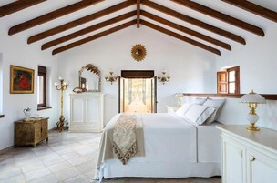 Un dormitorio con una cama grande, vigas de madera, un espejo, un aparador y una ventana.