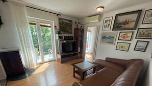 Una sala de estar con un sofá de cuero marrón, un televisor sobre un mueble de madera y un ventanal corredizo que da a un balcón.