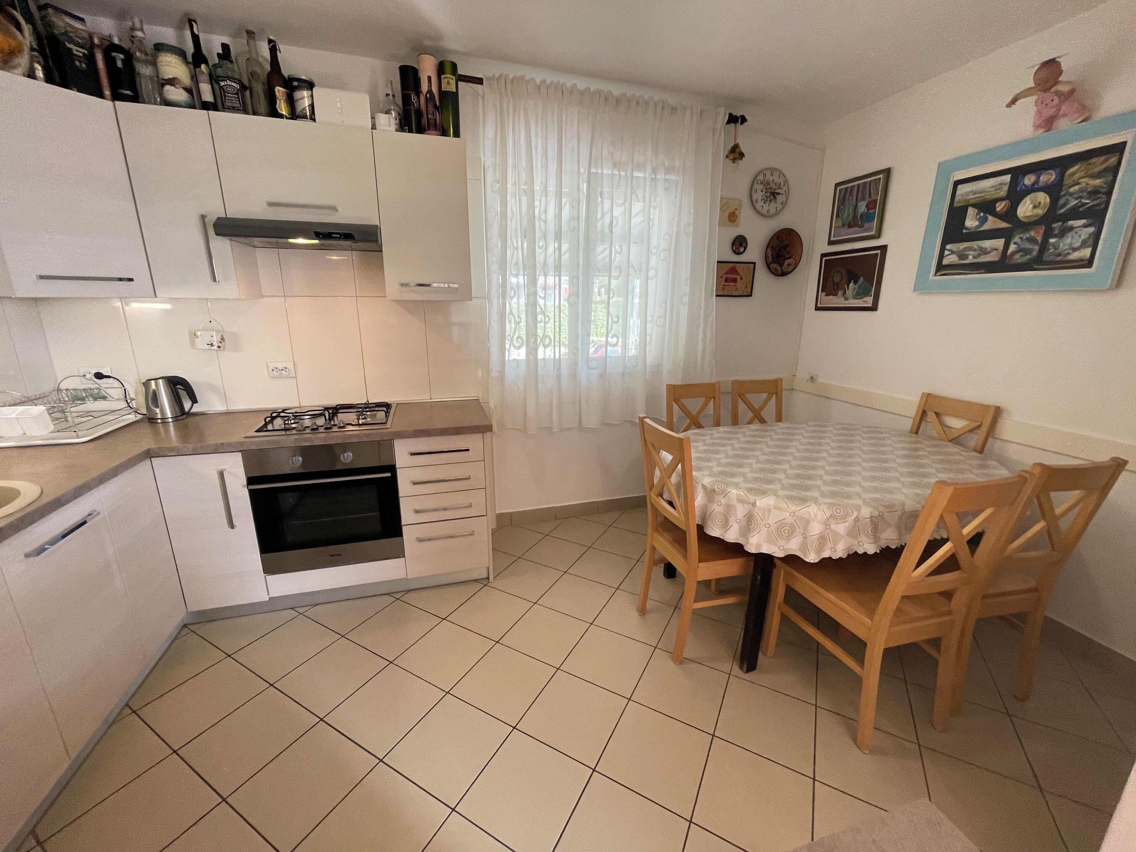 A compact kitchen with a gas stove, oven, and white cabinets. There is a dining table with wooden chairs and a white tablecloth.