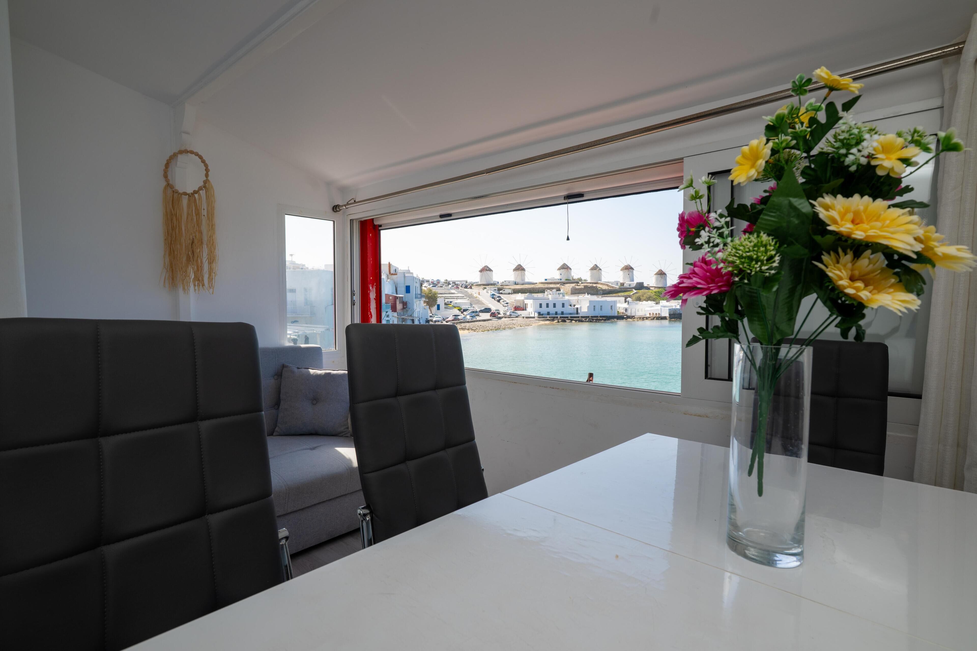 Ein modernes Zimmer mit großem Fenster, einem Tisch mit Blumenvase und Blick auf Windmühlen und Wasser.
