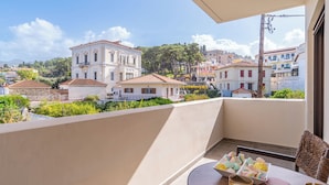 A balcony with a table, chairs, and a view of buildings and greenery. - Samos Tropic Apartments  (Samos)