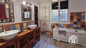 A bathroom with a large white bathtub, two sinks, and a mirror with decorative frames.