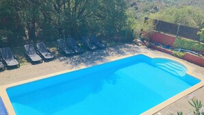 A rectangular swimming pool with a tiled edge, surrounded by lounge chairs and a stone deck.