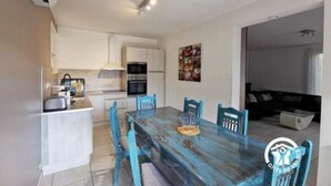 A modern kitchen with white cabinets, a built-in oven, and a dining area with a wooden table and blue chairs.