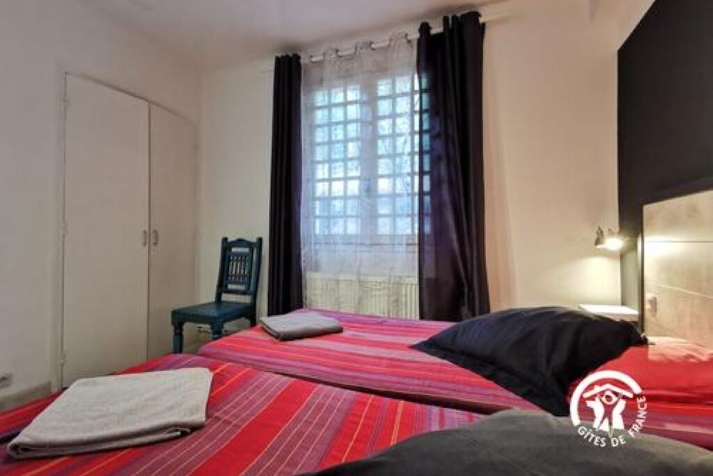 Un dormitorio con cama, una silla, armario y ventana con cortinas.