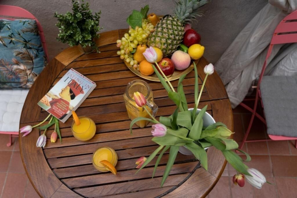 A round wooden table with a book, fruit, flowers, and a glass of juice.