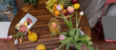 A round wooden table with a book, fruit, flowers, and a glass of juice.