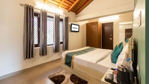 Habitación de hotel con cama, televisión, techo de madera y ventana con cortinas.