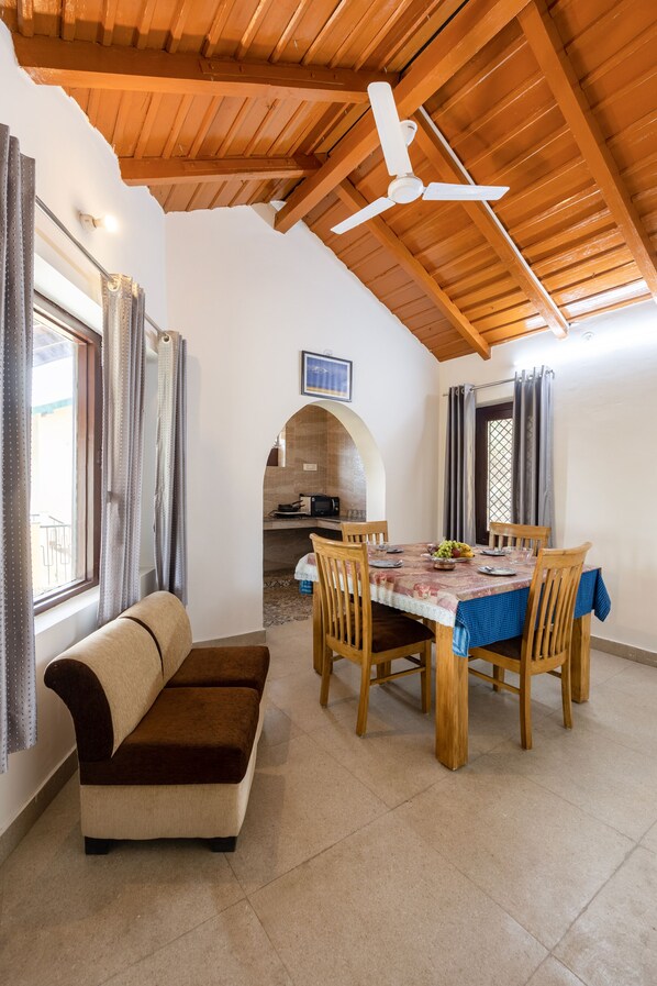 A dining area with a wooden table and chairs, a ceiling fan, and a view of the kitchen through an archway. - Divine Homes- Sattal By ASPL (Nainital)