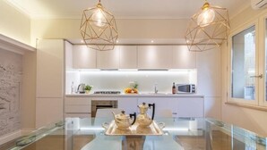 Een moderne keuken met witte kasten, een glazen eettafel en twee hanglampen.