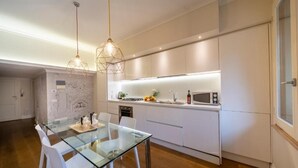 Een moderne keuken met witte kasten, een glazen eettafel en hanglampen.