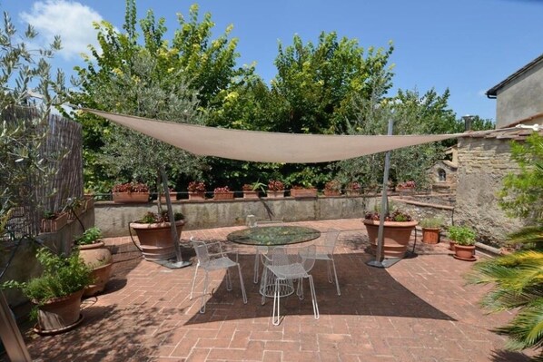 An outdoor patio with a round table and chairs, surrounded by potted plants and a shade sail.