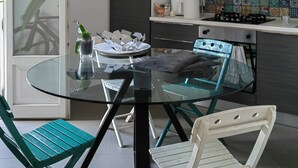 A modern kitchen with a glass dining table, teal chairs, and a variety of kitchen appliances. - Next to the massimo theater, beautiful apartment (Palermo)