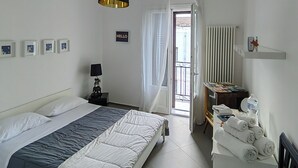 A hotel room with a bed, a bedside table with a lamp, a small table with towels, and a view of the outside balcony. - Next to the massimo theater, beautiful apartment (Palermo)