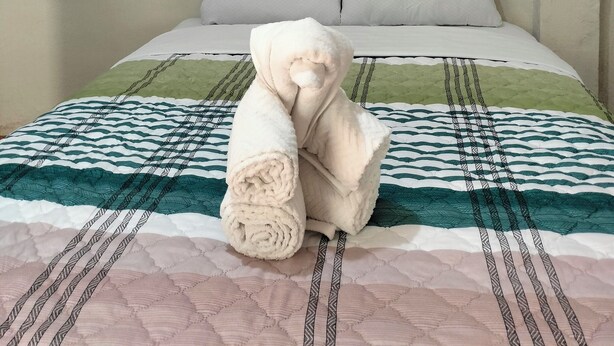 A neatly made bed with a patterned bedspread, a rolled towel, and a motivational quote on the wall.