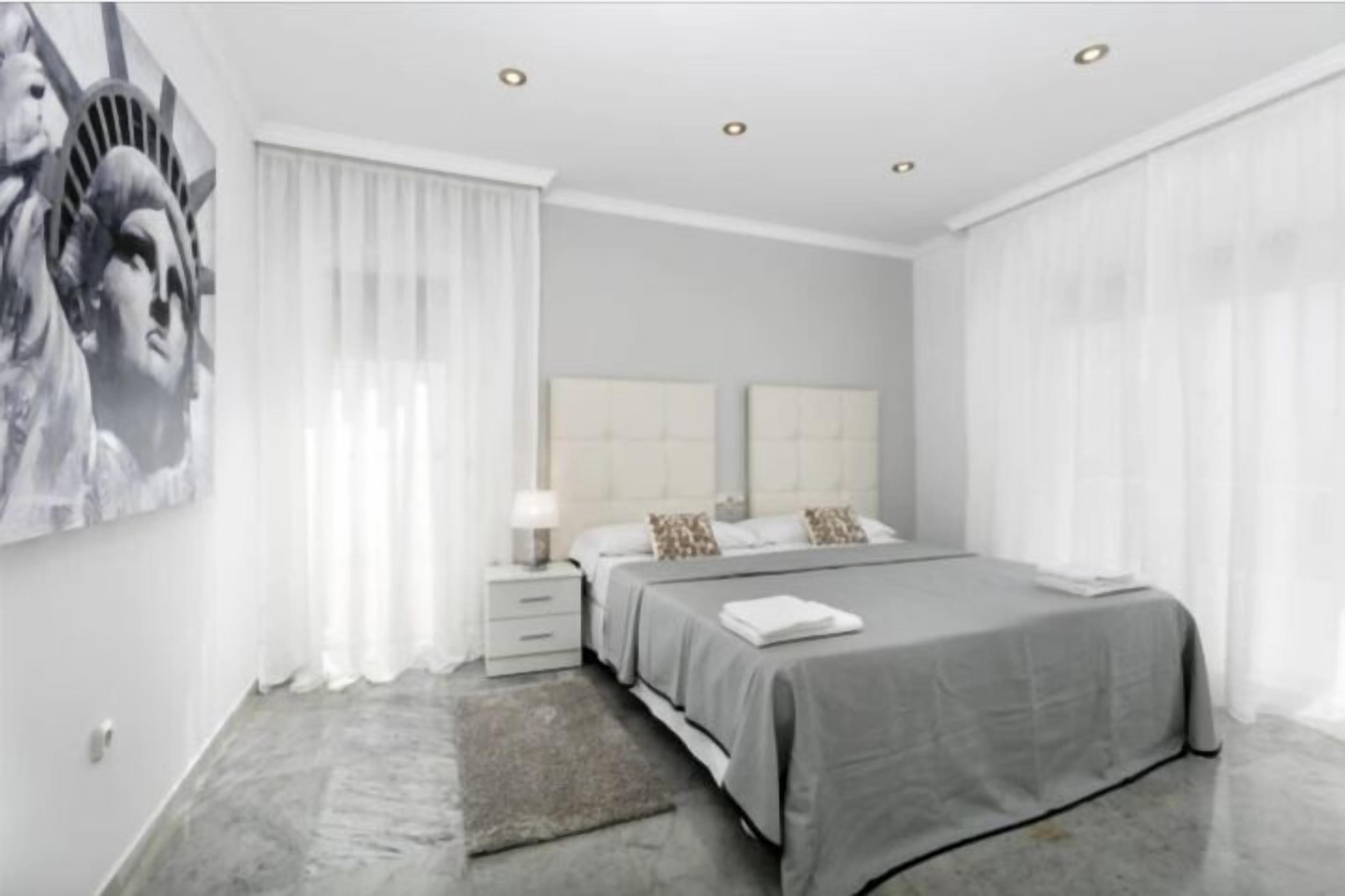 A modern bedroom with a large bed, a nightstand, and a wall-mounted artwork.