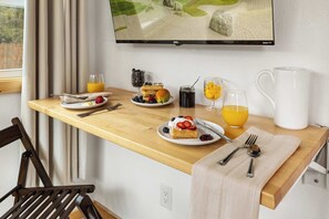 A breakfast setup with a wooden table, plates of food, glasses of juice, and a TV displaying a scenic view.