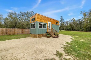 A small wooden cabin with a green exterior, a wooden deck, and a staircase leading to the entrance.