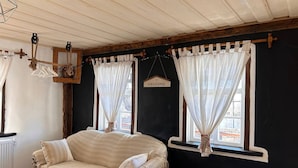 Une pièce avec un canapé, deux fenêtres avec des rideaux, une pancarte « BIENVENUE » et un plafond en bois.