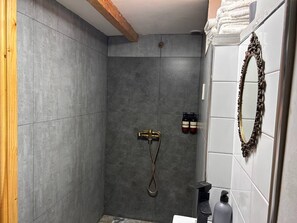 Shower area features a handheld showerhead and faucet, surrounded by large, square tiles and a wooden beam.