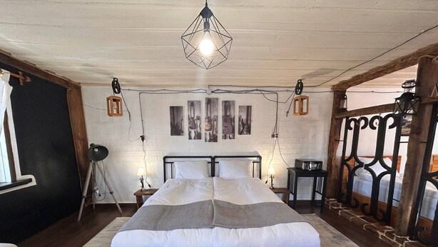 Une chambre à coucher avec un lit en bois, une tête de lit blanche et un luminaire au design géométrique.