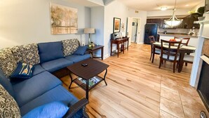Una sala de estar con un sofá azul, una mesa de centro y un comedor con suelo de madera y sillas.