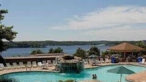 Un área de piscina con sillones reclinables, fuente de agua y vistas a un lago.