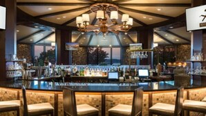 A bar area with a high ceiling, multiple chandeliers, and a bar stocked with various bottles. - Bogey Bungalow-Four Seasons-1BD/1BA/Balcony/Pool/Golf-2PP (Lake Ozark)