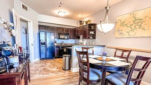 A modern kitchen with dark wooden cabinets, a stainless steel refrigerator, and a dining area with a wooden table and chairs. - Bogey Bungalow-Four Seasons-1BD/1BA/Balcony/Pool/Golf-2PP (Lake Ozark)