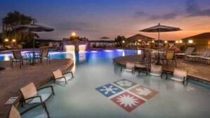 An outdoor swimming pool area with lounge chairs and umbrellas, surrounded by buildings. - Bogey Bungalow-Four Seasons-1BD/1BA/Balcony/Pool/Golf-2PP (Lake Ozark)