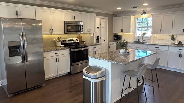 A modern kitchen with stainless steel appliances, white cabinetry, and a central island with bar stools. - Sleeps 6-8; Across from Sand Mountain Park (Albertville)