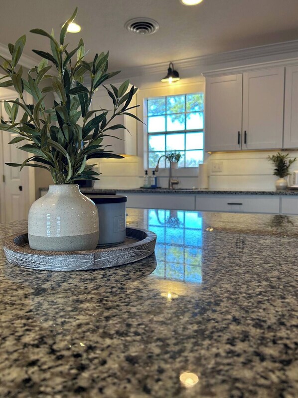 A kitchen with white cabinets, a granite countertop, and a potted plant on a round wooden tray.
