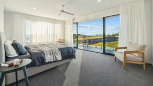 A modern bedroom with a large bed, a chair, a table, and a view of a landscape through large windows. - Elysium - Skennars Head (Skennars Head)