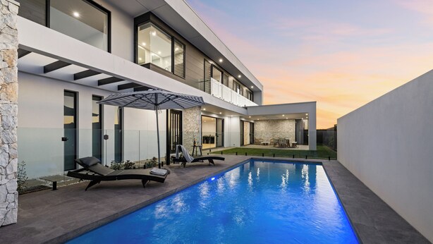 A modern house with a swimming pool, outdoor seating, and a well-lit balcony. - Elysium - Skennars Head (Skennars Head)