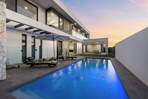 A modern house with a swimming pool, outdoor seating, and a well-lit balcony.