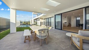 A modern outdoor patio with a dining table and chairs, a pool, and a view of the house interior. - Elysium - Skennars Head (Skennars Head)