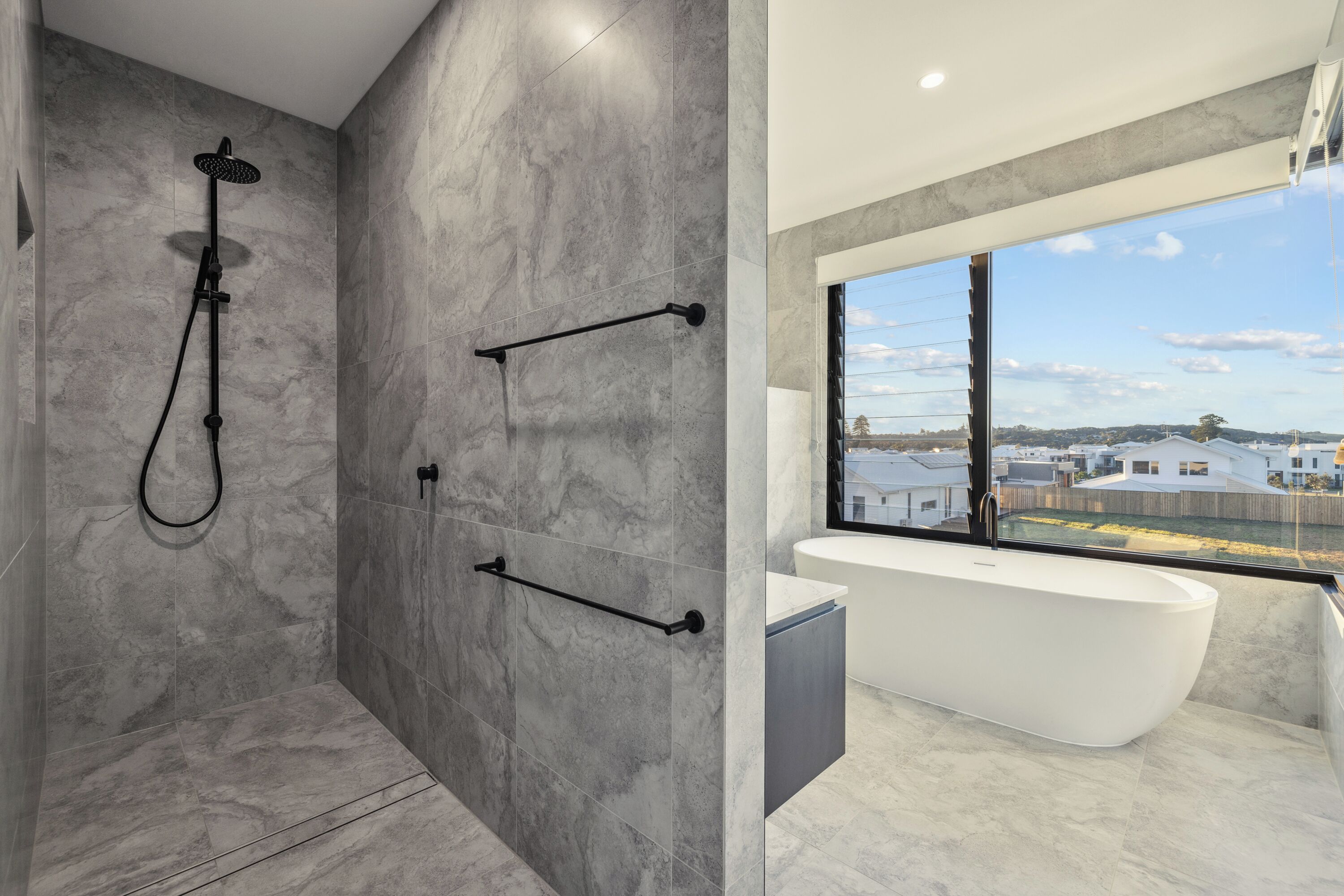 Une salle de bain moderne dotée d’une douche, d’une baignoire et d’une grande fenêtre donnant sur les environs.