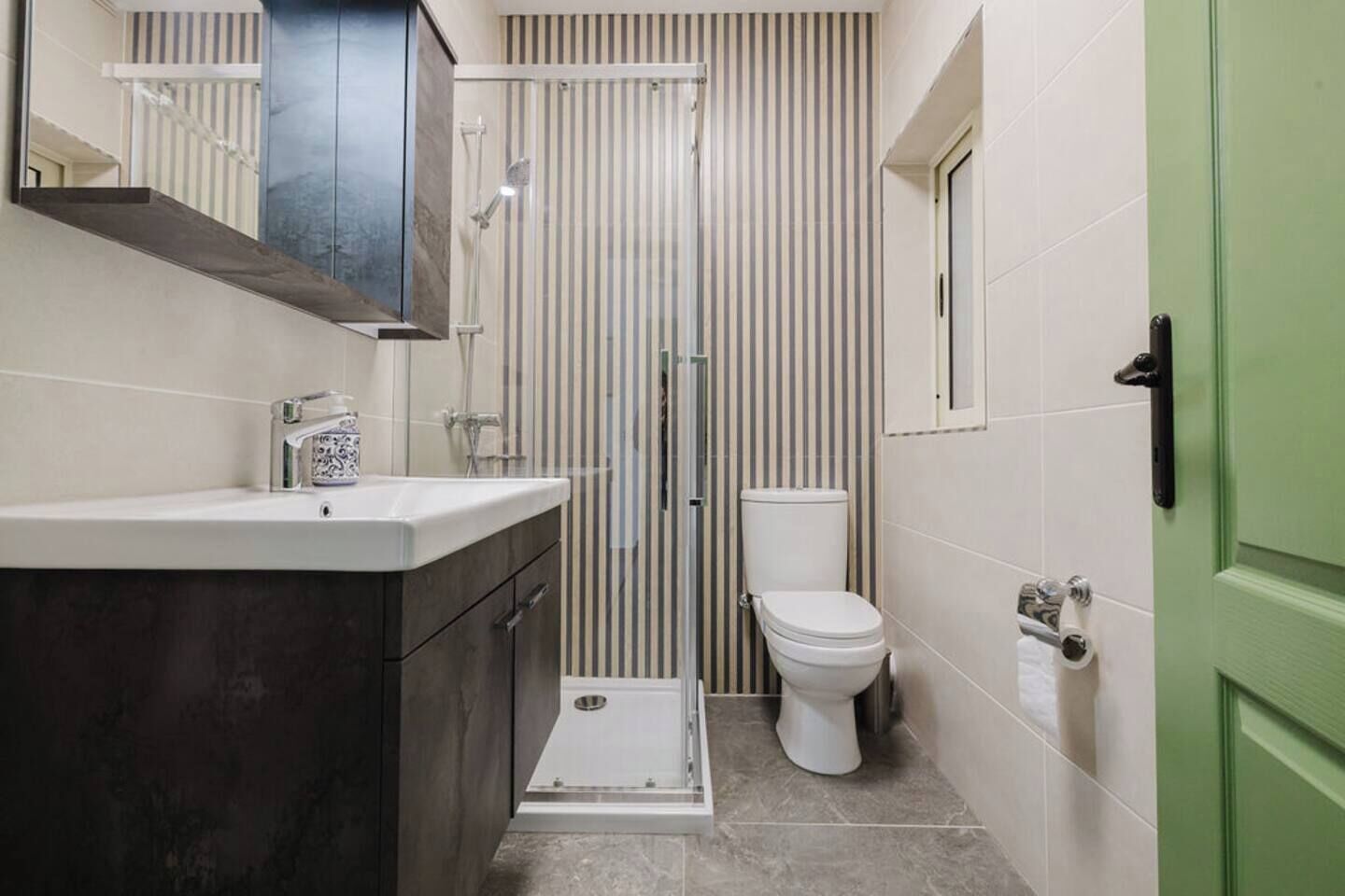 Un baño compacto con ducha, inodoro y lavabo con un mueble oscuro.